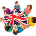 Top view of seven kids holding English flag in the middle of their circle, isolated on white background